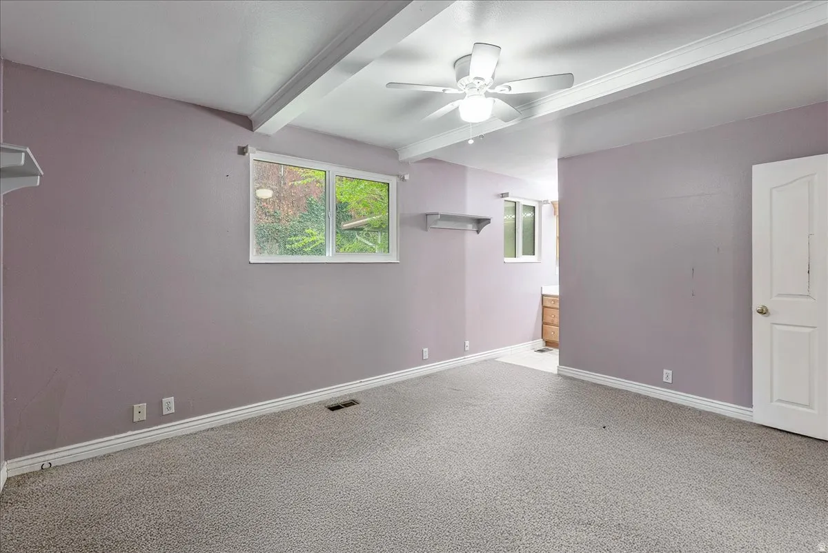 Empty room featuring beam ceiling, ceiling fan, and light carpet