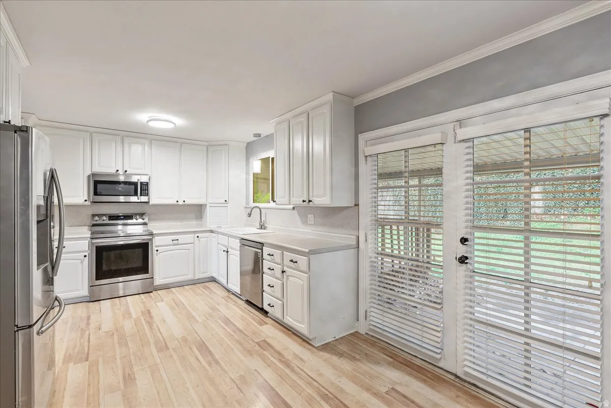 Kitchen featuring white cabinets, stainless steel appliances, light countertops, light wood-type flooring, and crown molding