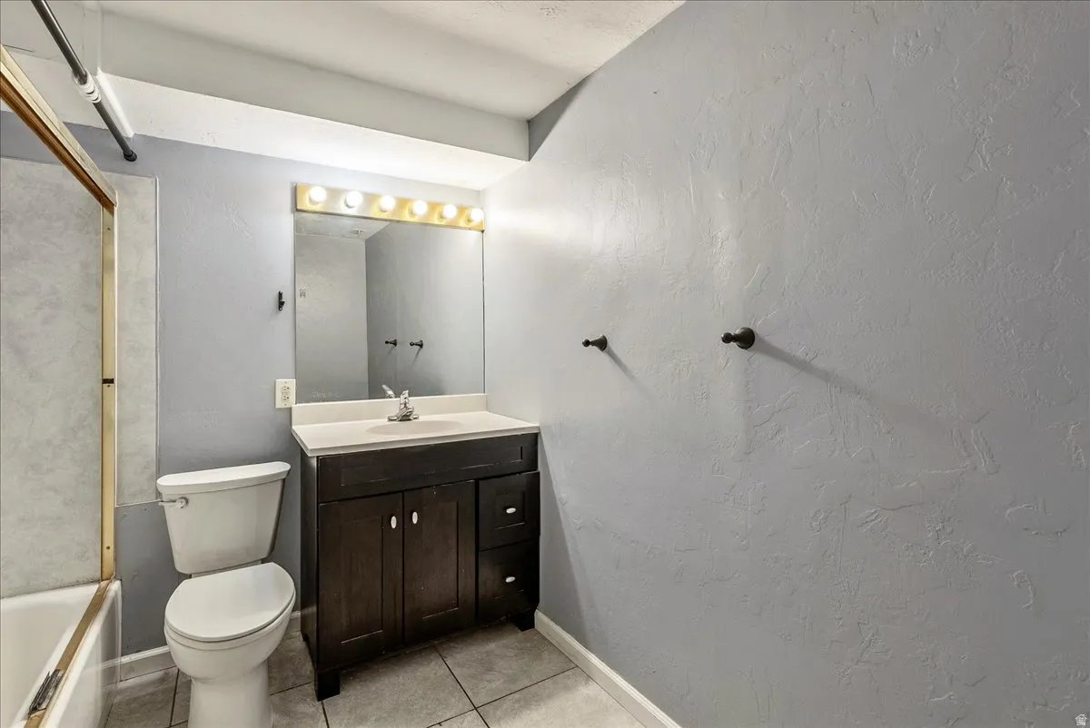 Full bathroom featuring a textured wall, vanity, light tile patterned floors, and shower / bathtub combination