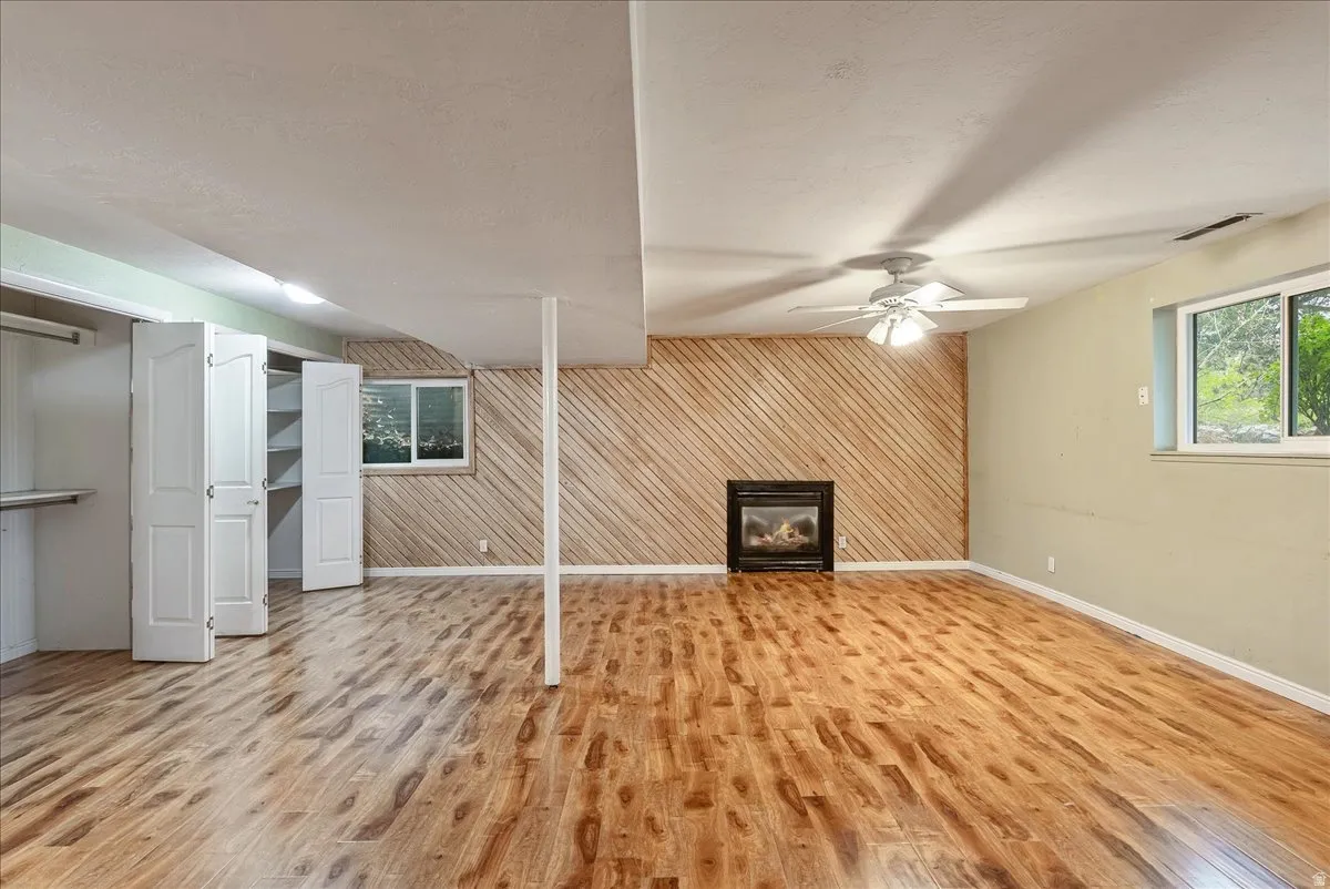 Unfurnished living room with wood walls, a glass covered fireplace, light wood-style floors, an accent wall, and a ceiling fan