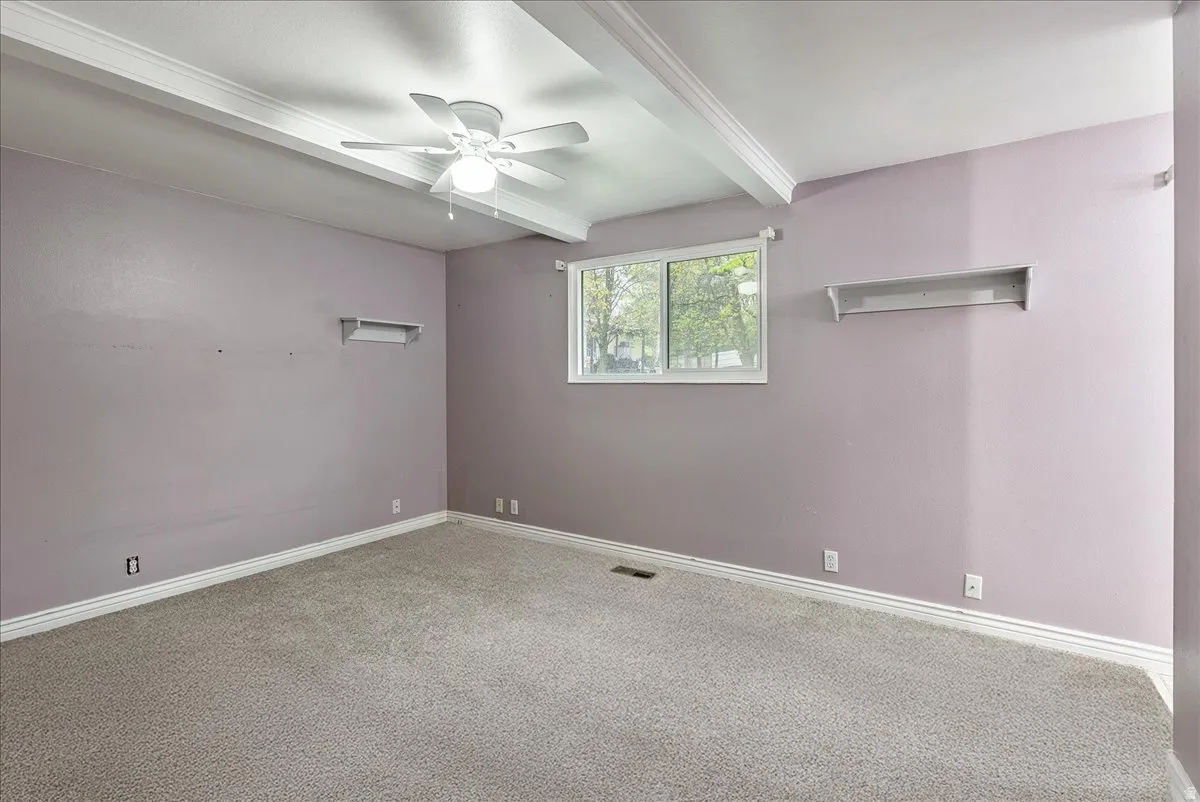 Empty room featuring beamed ceiling, ceiling fan, and carpet flooring