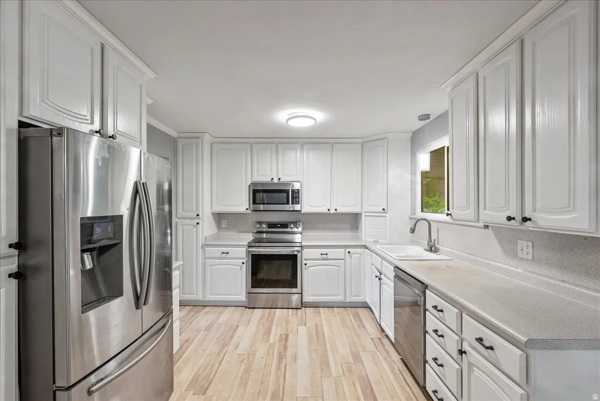 Kitchen featuring stainless steel appliances, white cabinetry, light countertops, and light wood finished floors