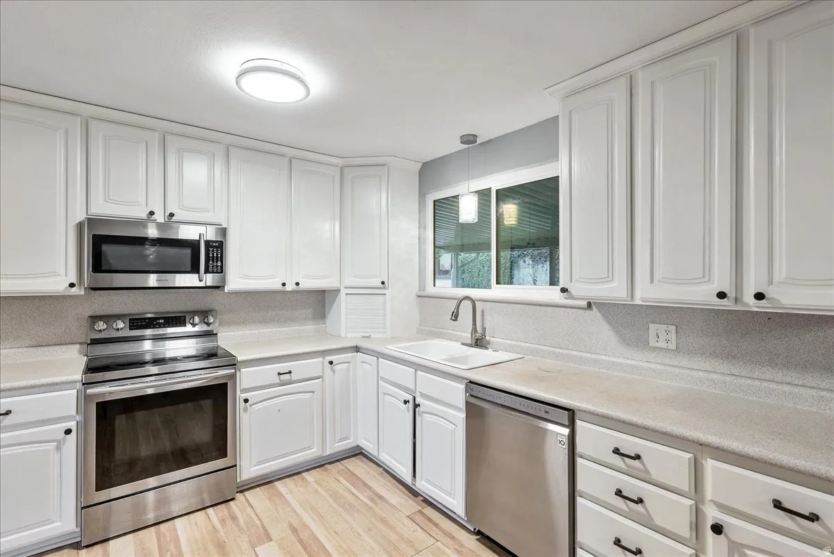 Kitchen featuring stainless steel appliances, white cabinets, light countertops, and light wood-style flooring