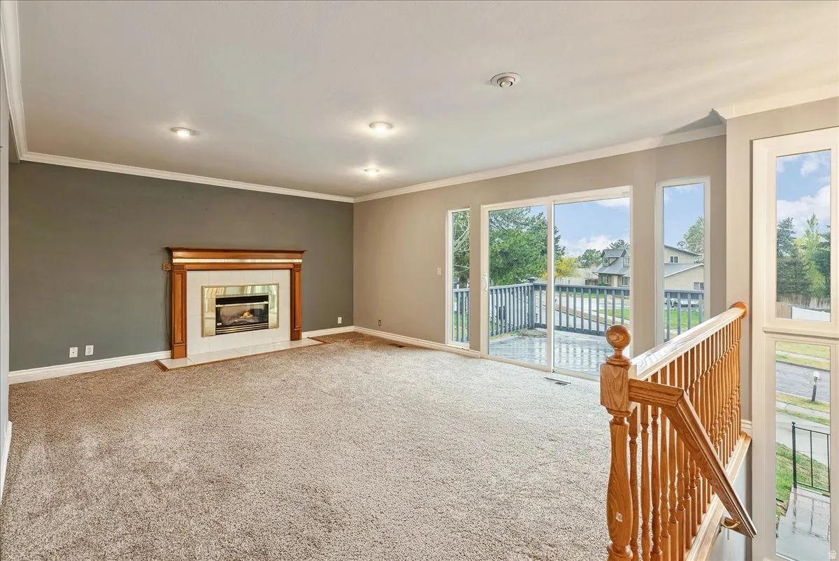 Unfurnished living room featuring carpet, a tiled fireplace, and ornamental molding