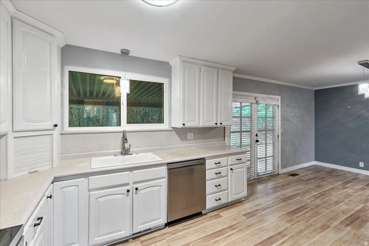 Kitchen featuring pendant lighting, stainless steel dishwasher, white cabinetry, and crown molding