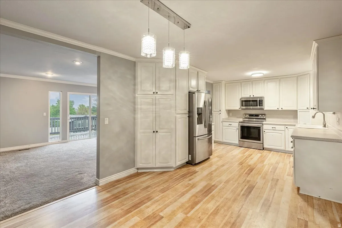Kitchen featuring crown molding, stainless steel appliances, light countertops, light wood-style floors, and white cabinetry