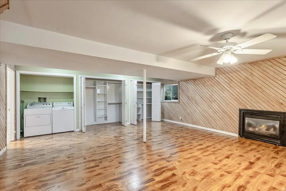 Finished below grade area with a glass covered fireplace, independent washer and dryer, light wood-type flooring, wooden walls, and ceiling fan