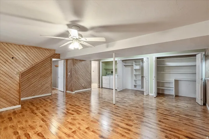 Unfurnished living room with ceiling fan, wooden walls, light wood-type flooring, and independent washer and dryer