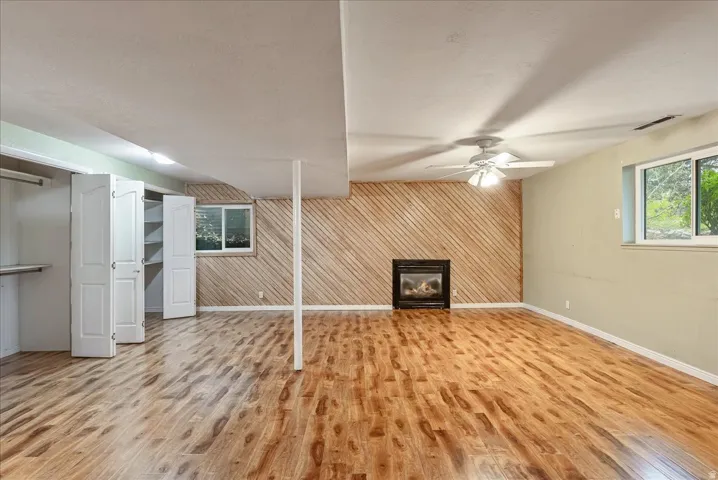 Unfurnished living room with wood walls, a glass covered fireplace, light wood-style floors, an accent wall, and a ceiling fan