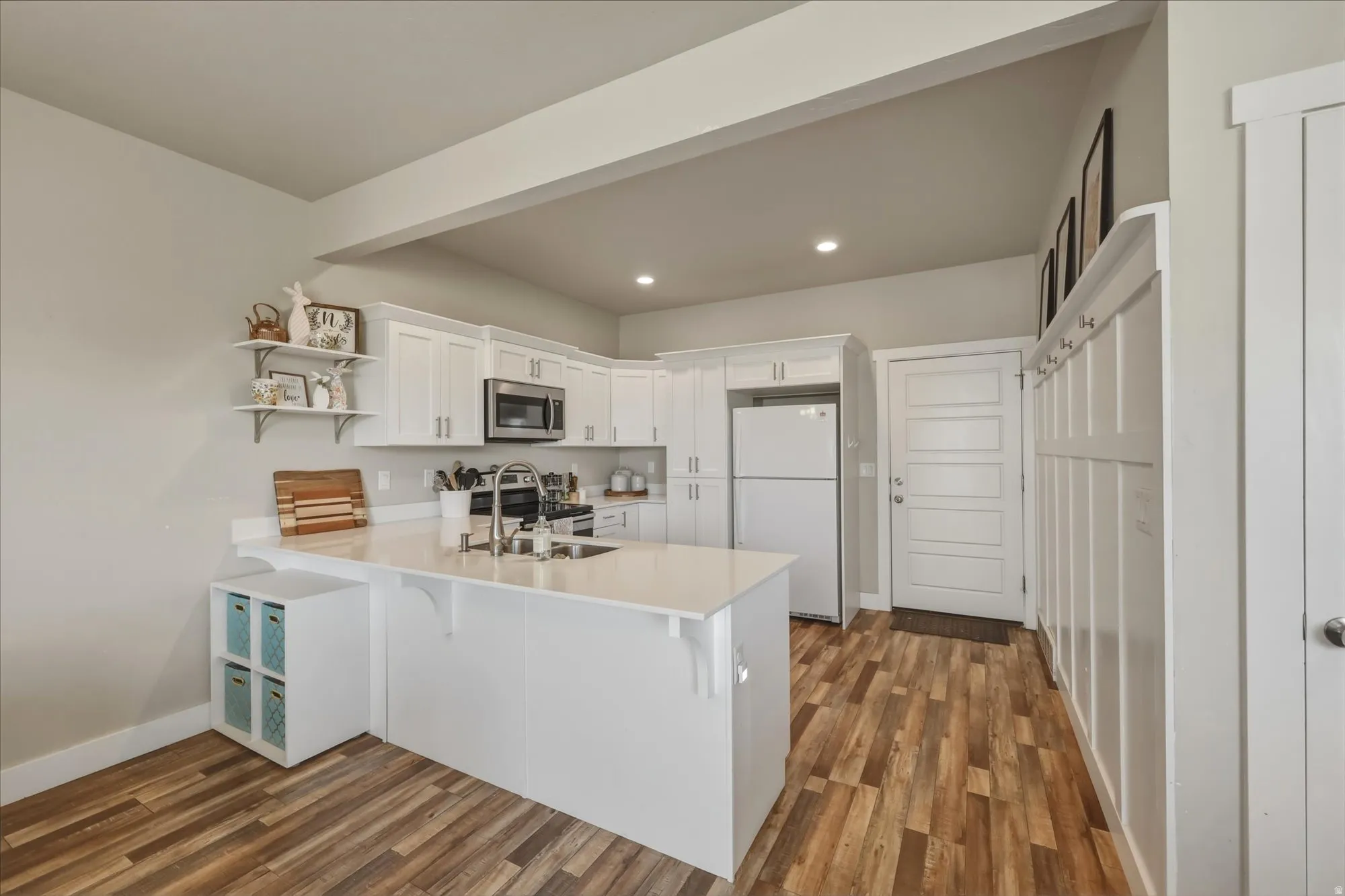 Kitchen with white cabinets, stainless steel appliances, open shelves, a peninsula, and dark wood-style flooring