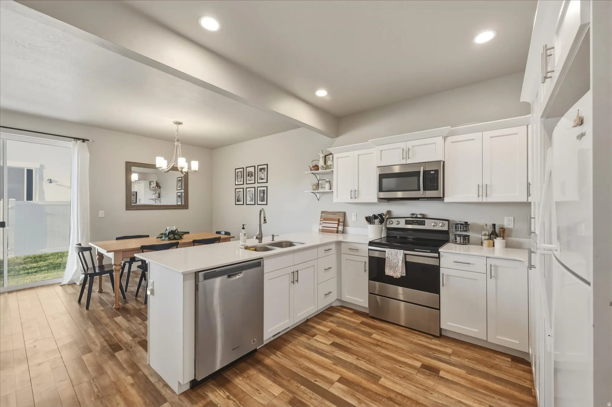 Kitchen with a peninsula, stainless steel appliances, white cabinetry, and light wood finished floors