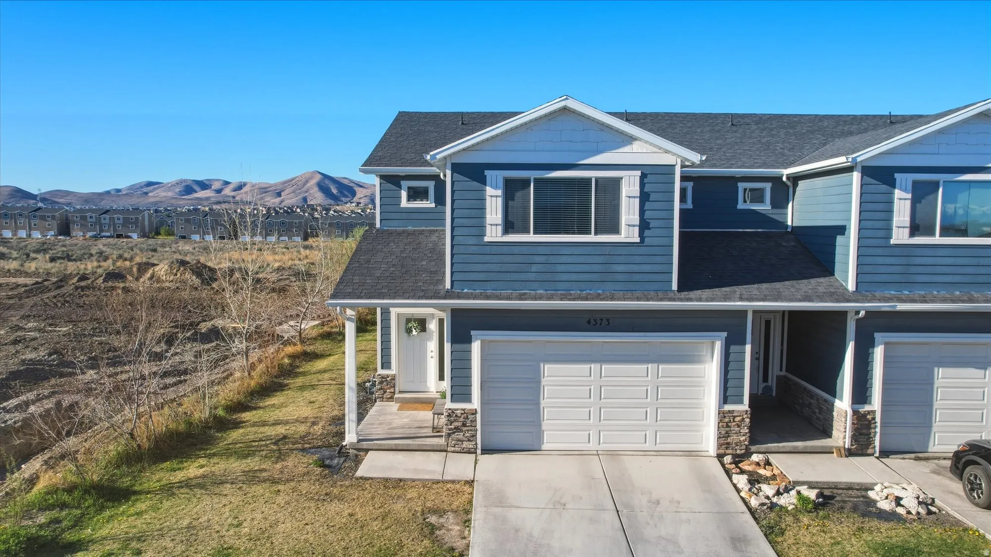 View of front of home featuring stone siding, a shingled roof, concrete driveway, and an attached garage