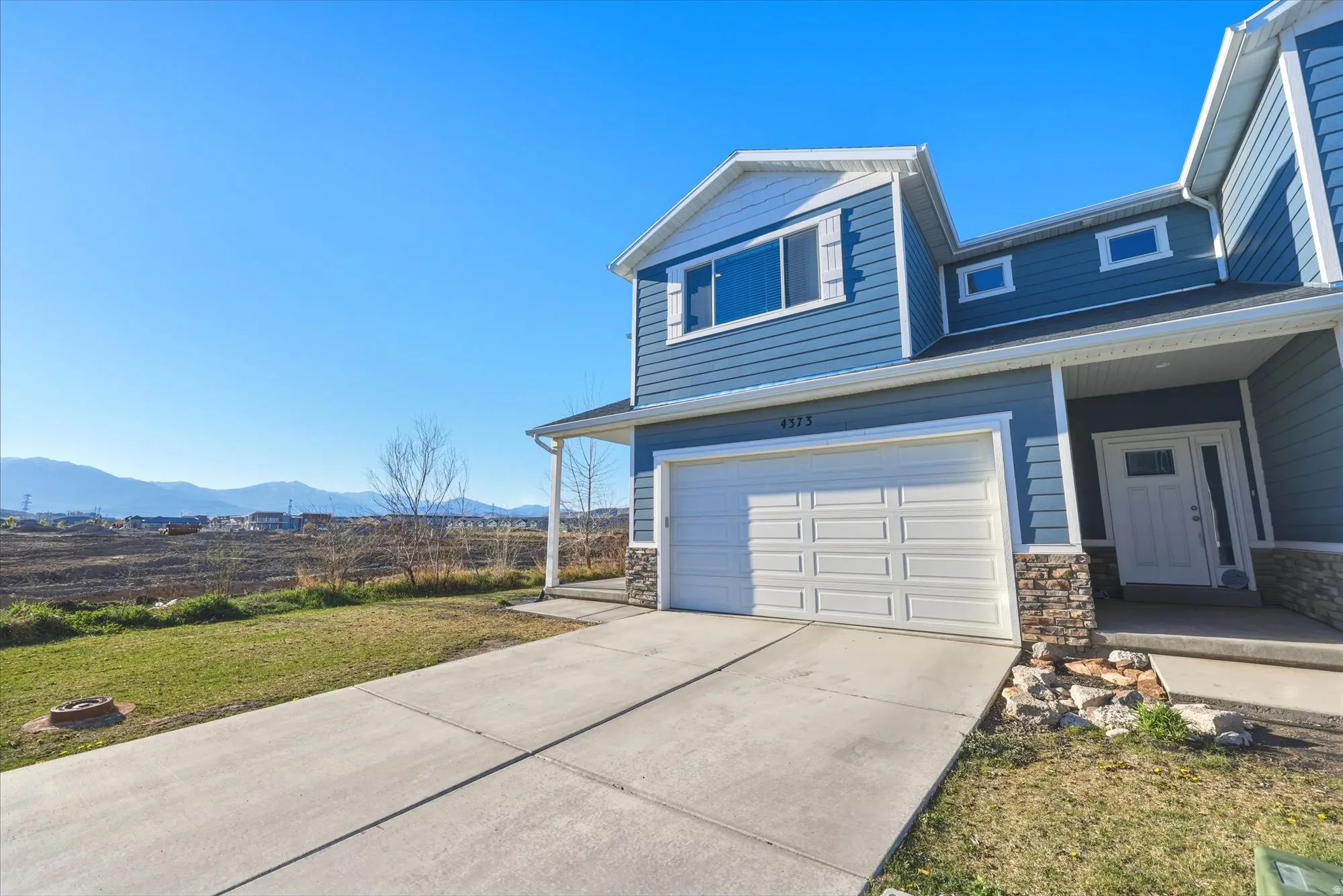 View of front of home featuring stone siding, a mountain view, a garage, driveway, and a front yard