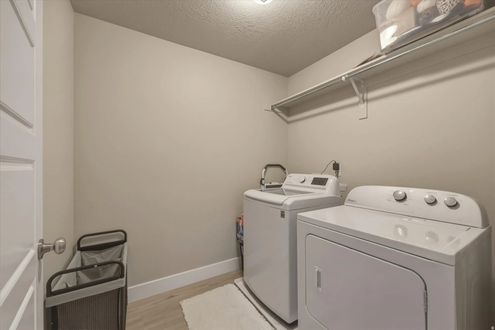 Laundry room featuring a textured ceiling, light wood-style floors, and washer and clothes dryer