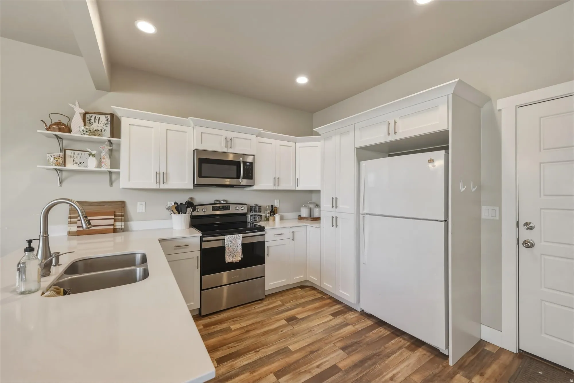 Kitchen with open shelves, stainless steel appliances, white cabinets, dark wood-type flooring, and light stone countertops