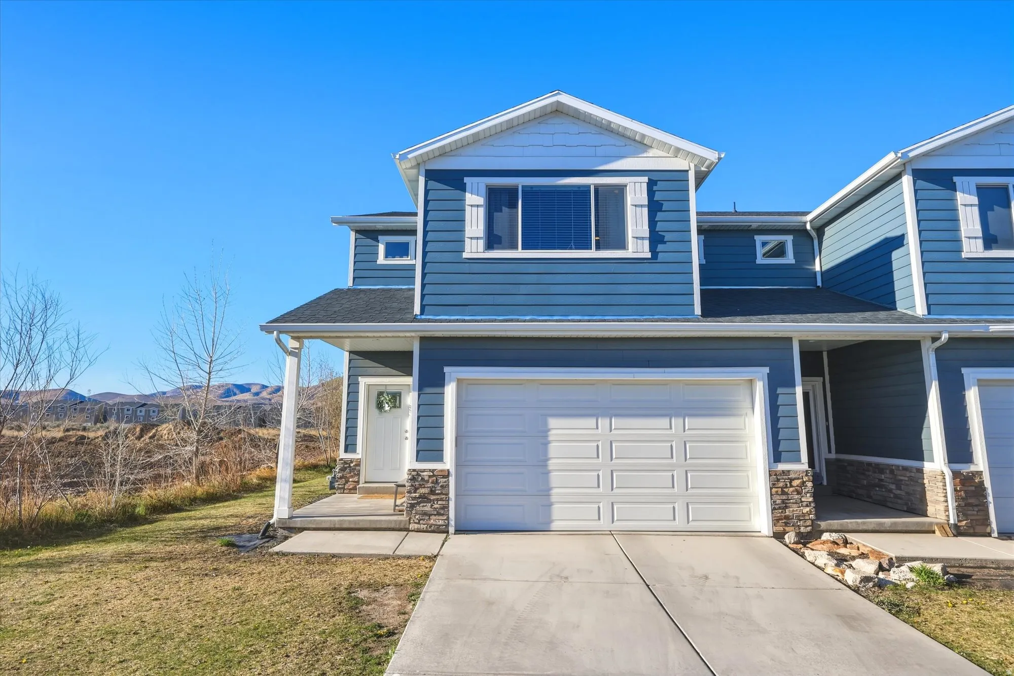 View of front of house with stone siding, a garage, concrete driveway, and a front lawn