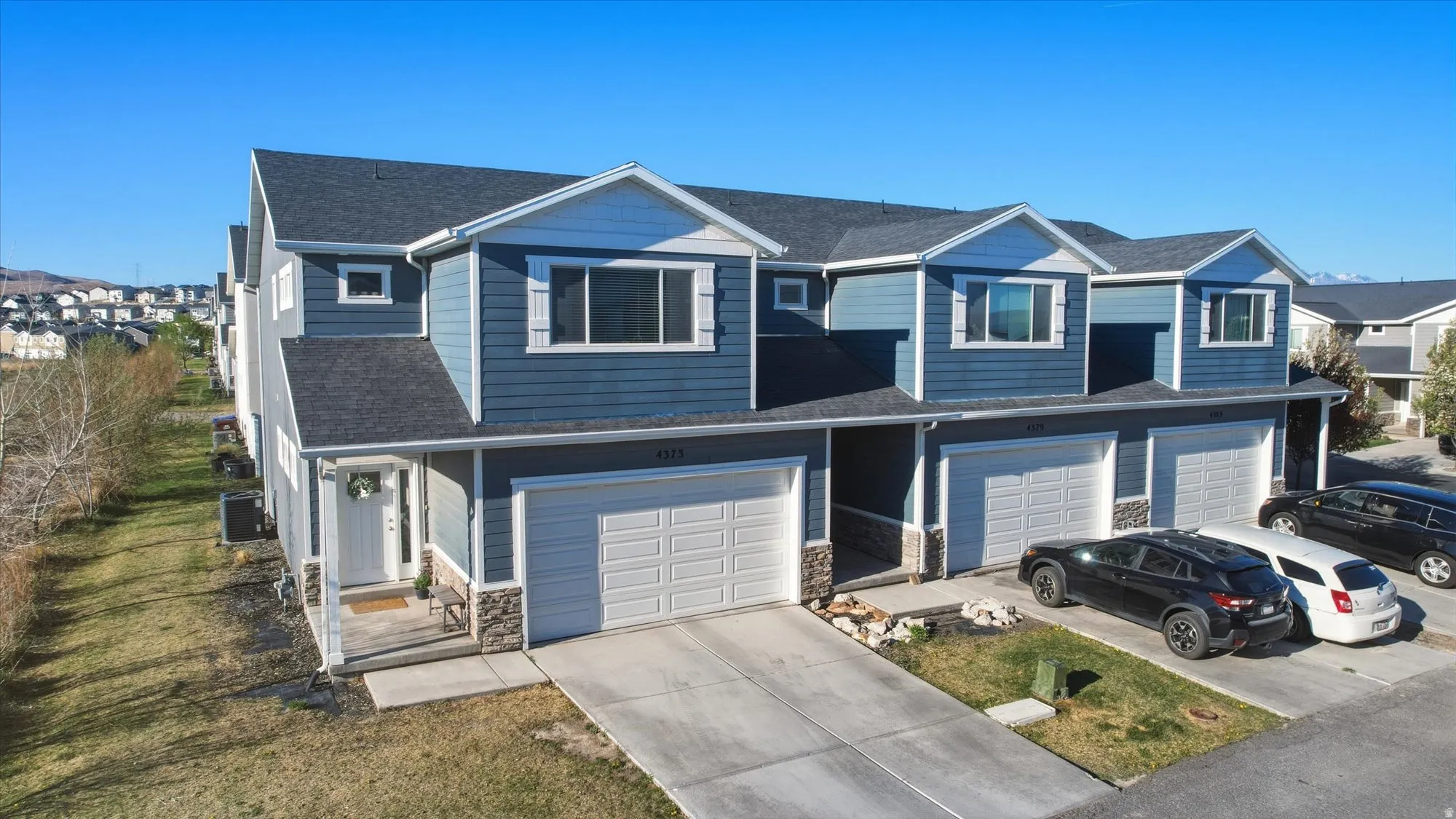 View of front of home featuring stone siding, roof with shingles, driveway, a residential view, and a garage