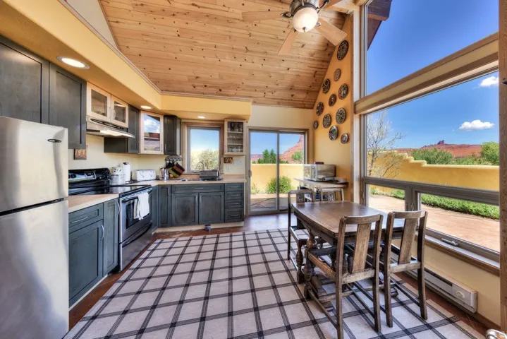 Kitchen featuring a vaulted wooden ceiling, stainless steel appliances, light countertops, glass insert cabinets, and ceiling fan