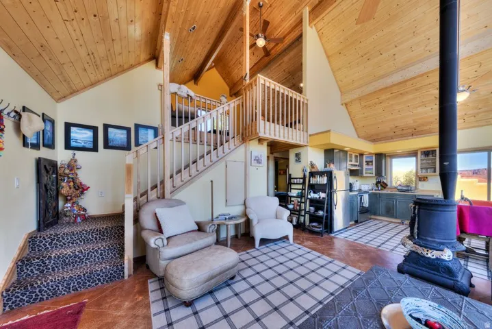 Living room with a high wooden beamed ceiling, a wood stove, and ceiling fan