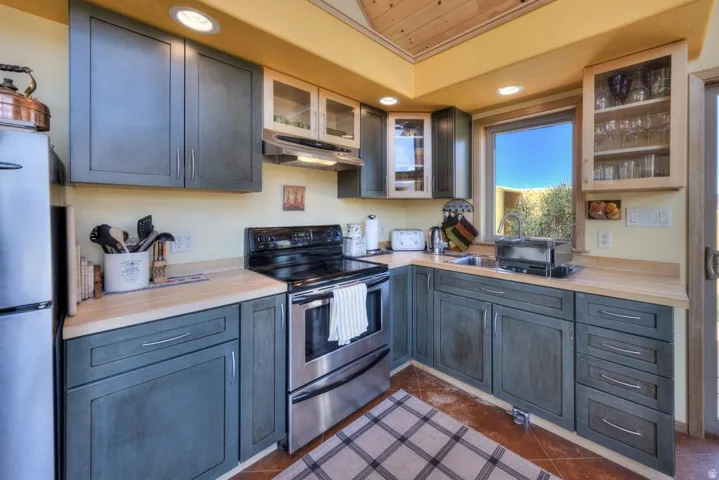 Kitchen with glass insert cabinets, stainless steel electric range, freestanding refrigerator, recessed lighting, and gray cabinetry