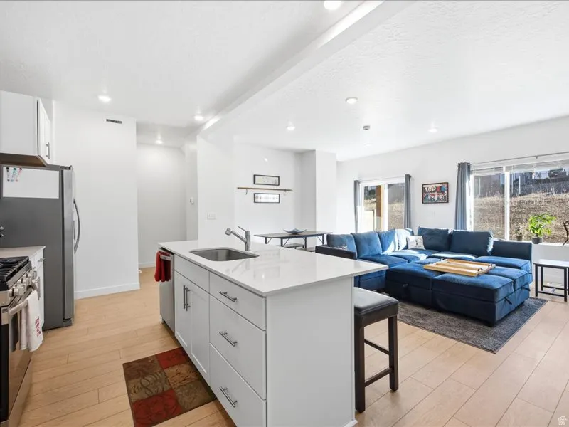 Kitchen with a kitchen bar, white cabinetry, lvp flooring, quartzite countertops, center island with sink and pantry.
