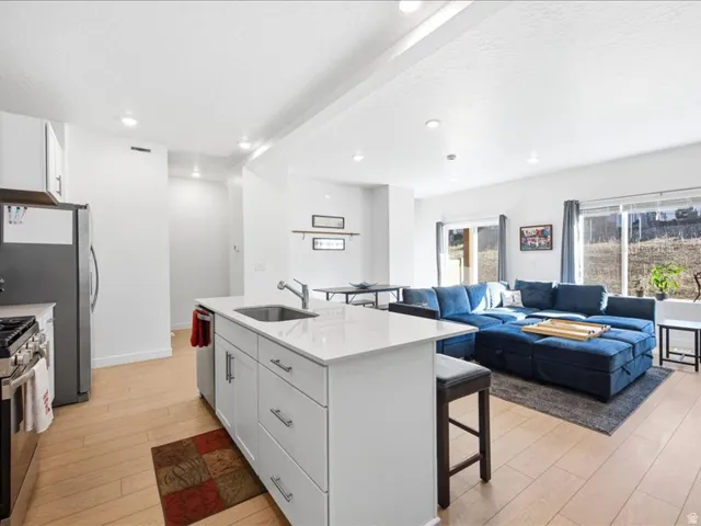 Kitchen with a kitchen bar, white cabinetry, lvp flooring, quartzite countertops, center island with sink and pantry.