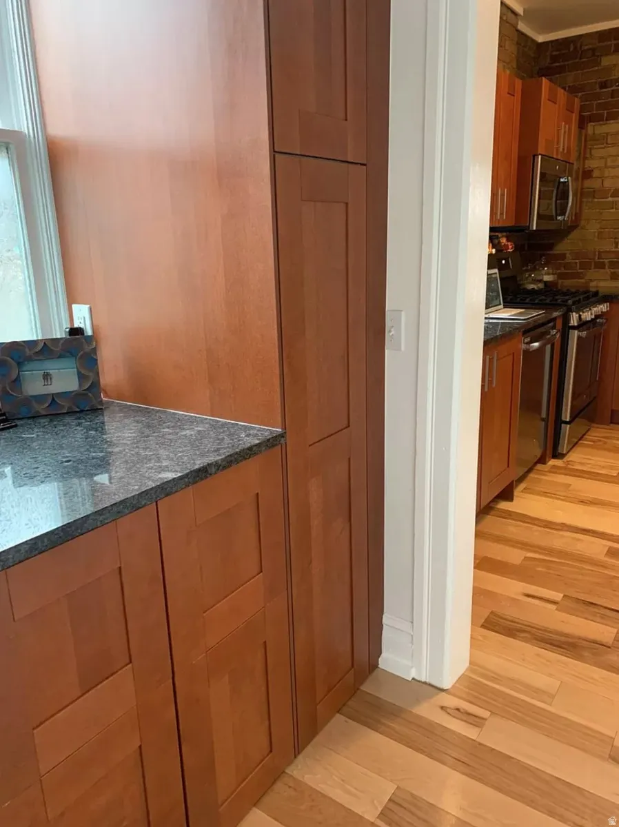 Kitchen with wood finish cabinetry, dark stone counters, light wood finished floors, stainless steel appliances, and tasteful backsplash