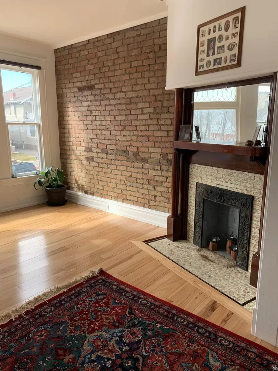 Unfurnished living room with wood finished floors, a fireplace with flush hearth, and brick wall