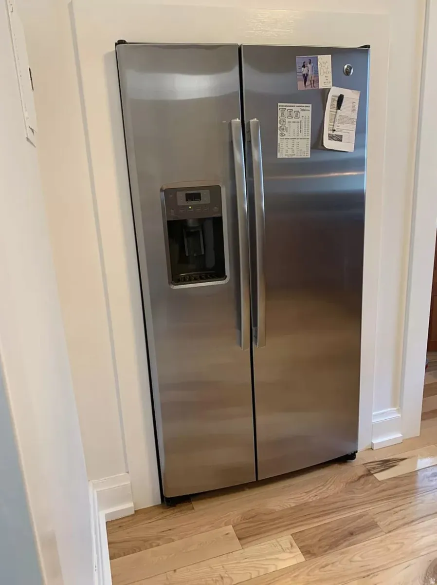 Kitchen view of stainless steel refrigerator with ice dispenser and light wood-style floors