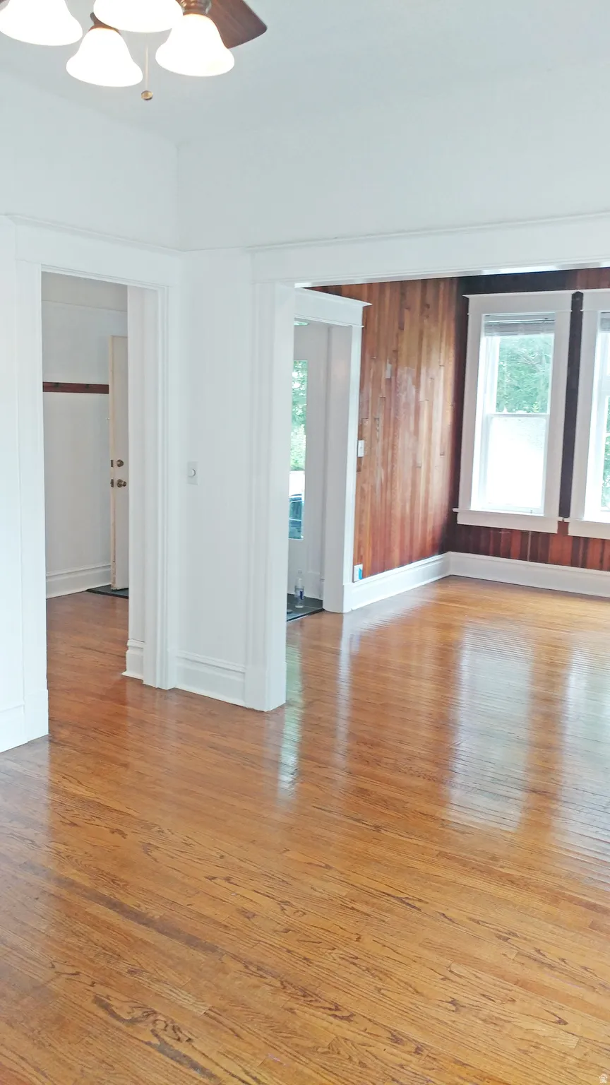 Spare room featuring light wood-style flooring, plenty of natural light, a ceiling fan, and wood walls