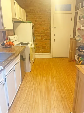 Kitchen featuring white appliances, light wood finished floors, brick wall, white cabinetry, and dark countertops
