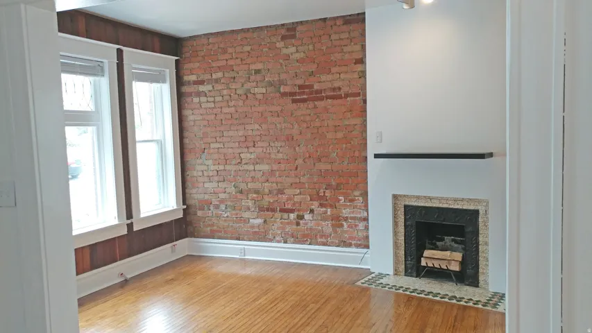 Unfurnished living room featuring brick wall, light wood finished floors, and a fireplace with flush hearth