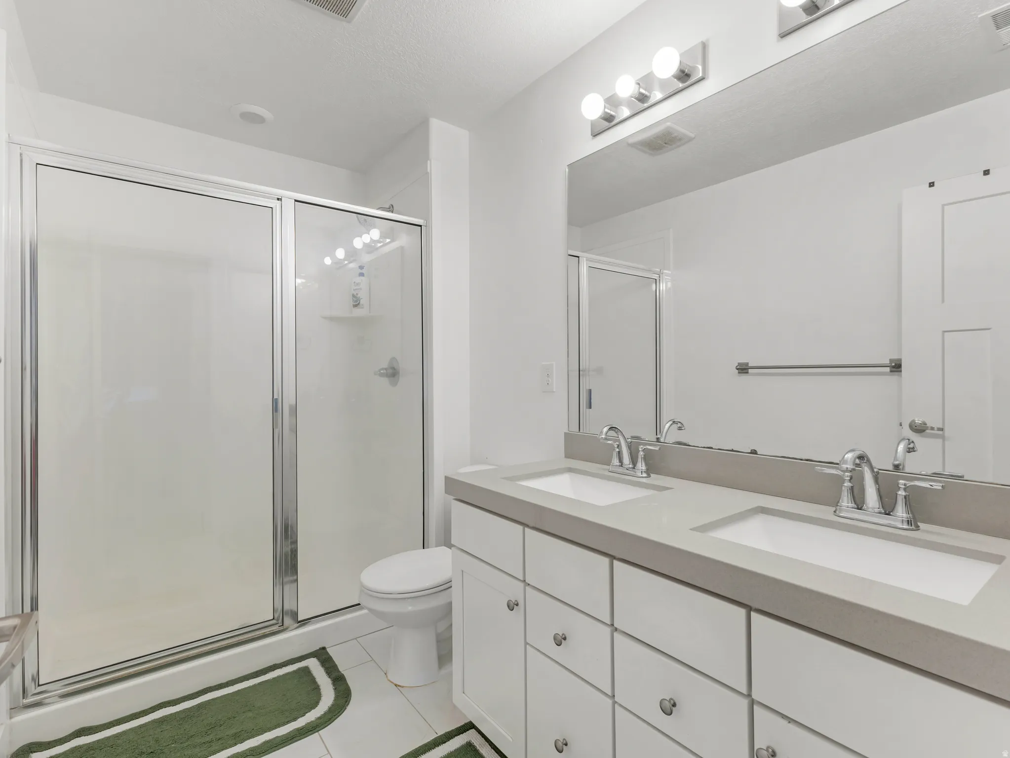 Bathroom with double vanity, a shower stall, and light tile patterned flooring