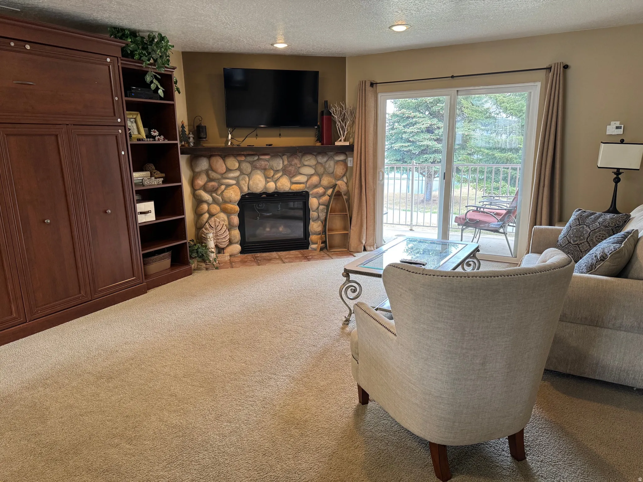 Living room featuring carpet flooring, a textured ceiling, a stone fireplace, and recessed lighting