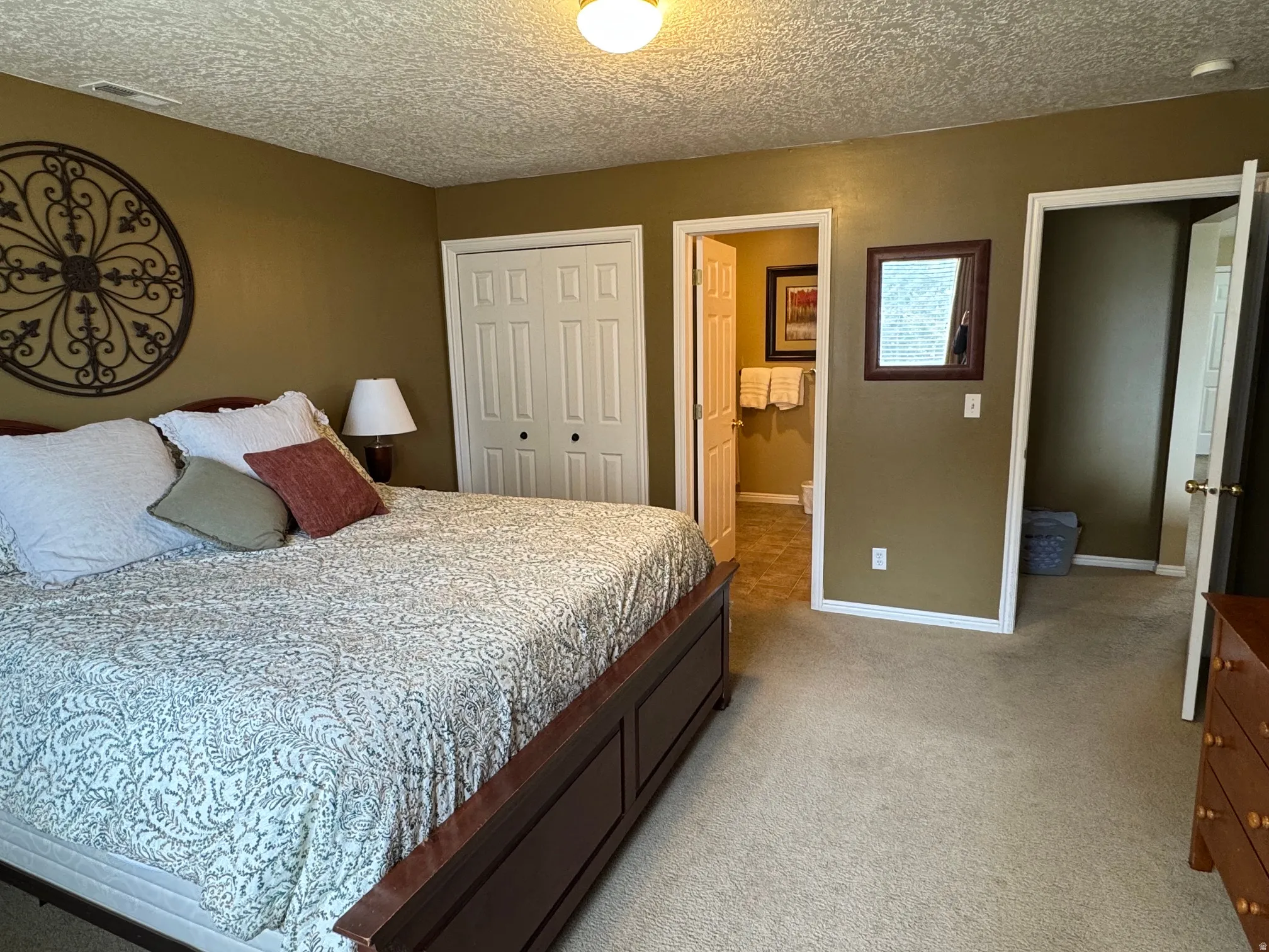 Bedroom featuring light colored carpet, a textured ceiling, a closet, and connected bathroom