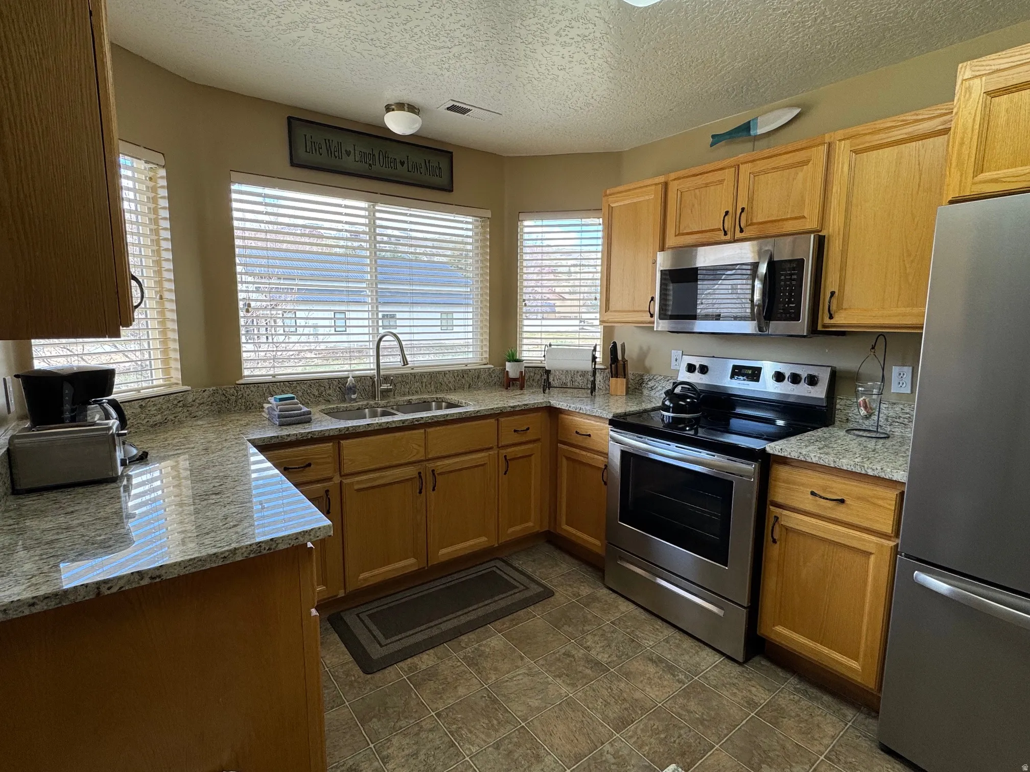 Kitchen with stainless steel appliances, light stone countertops, and a textured ceiling