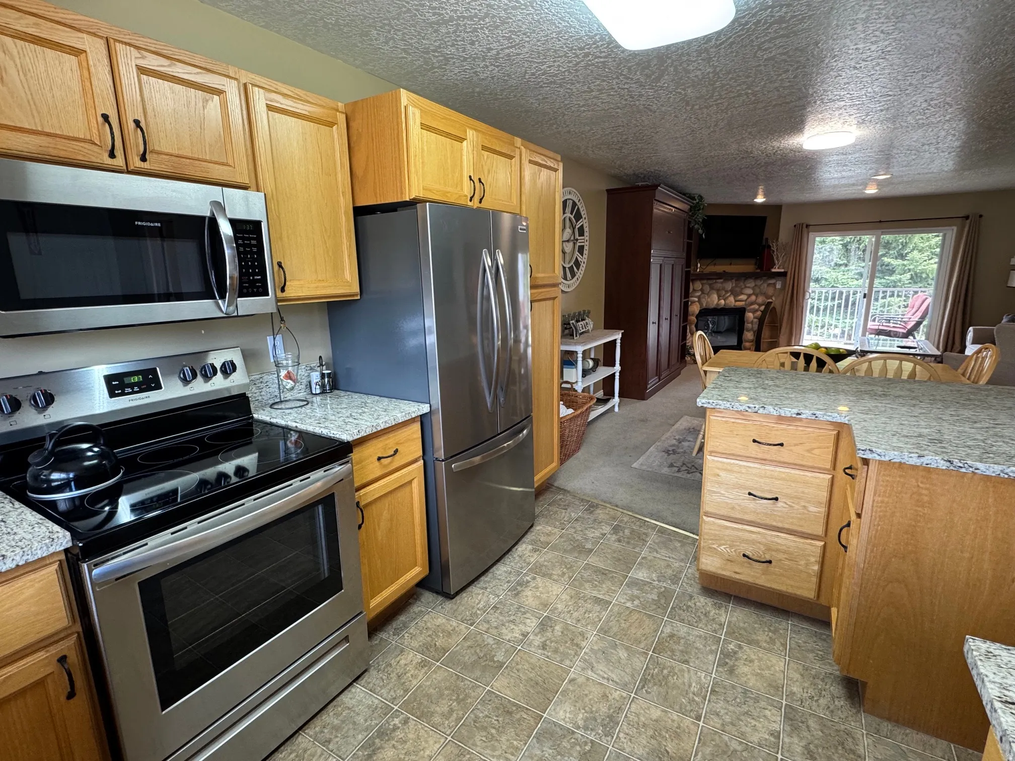 Kitchen with stainless steel appliances, a stone fireplace, a textured ceiling, light stone countertops, and stone finish flooring
