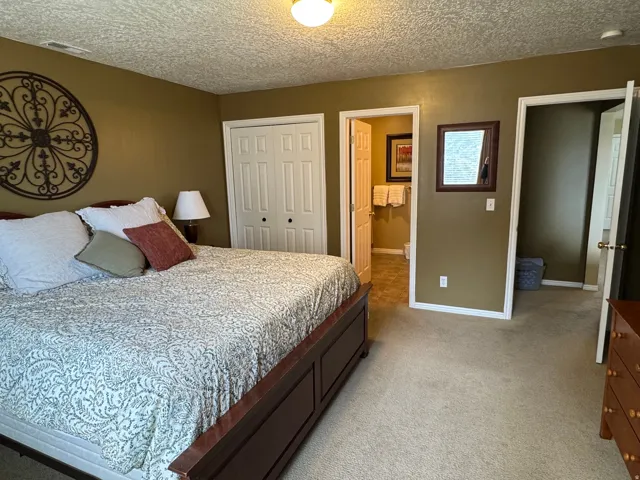 Bedroom featuring light colored carpet, a textured ceiling, a closet, and connected bathroom