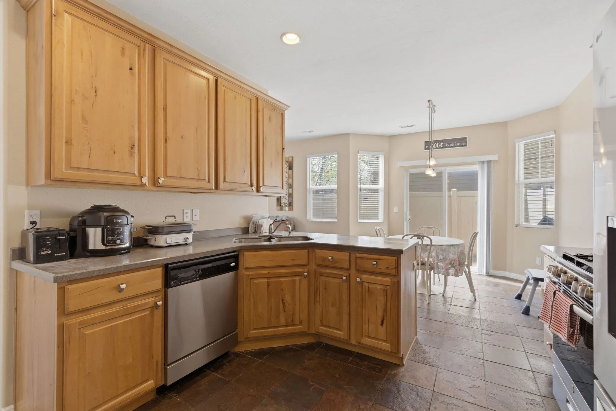 Kitchen featuring stone tile flooring, a peninsula, stainless steel appliances, and pendant lighting