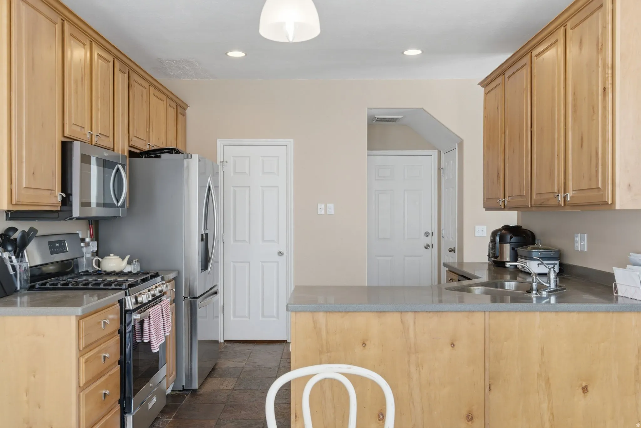 Kitchen with stainless steel appliances, a peninsula, light wood finish cabinets, stone tile flooring, and recessed lighting