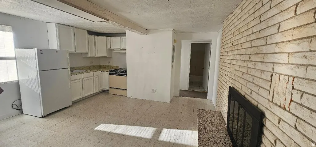 Kitchen featuring light flooring, white appliances, white cabinetry, brick wall, and a textured ceiling