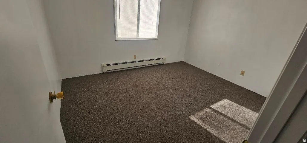 Empty room featuring dark carpet and baseboard heating