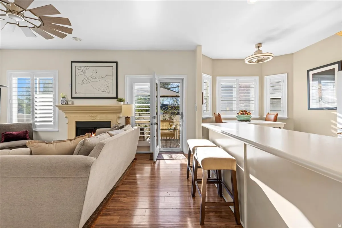 Living room featuring dark wood finished floors, a ceiling fan, and a warm lit fireplace