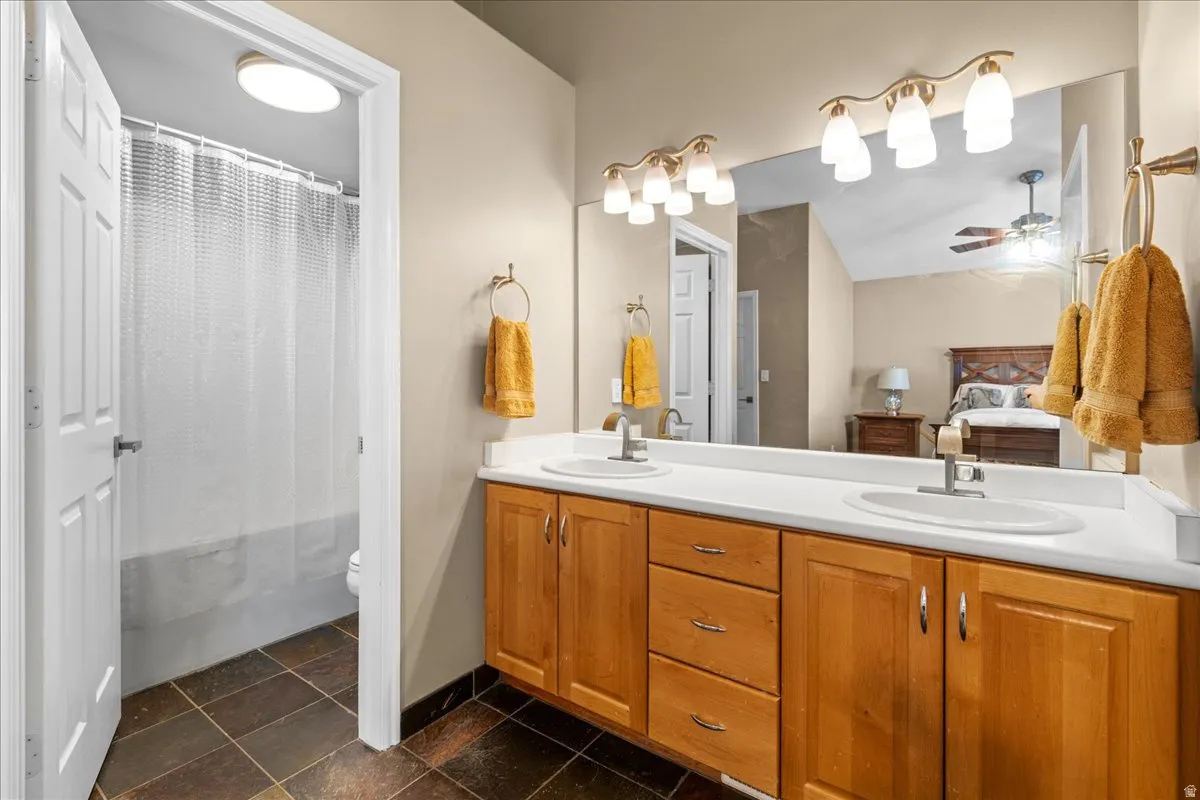 Full bath featuring connected bathroom, double vanity, ceiling fan, and shower / tub combo with curtain