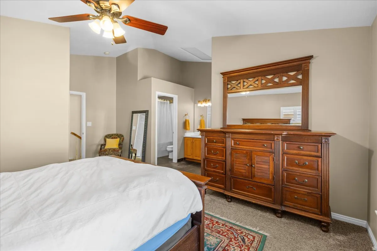 Bedroom with dark colored carpet, ceiling fan, and connected bathroom