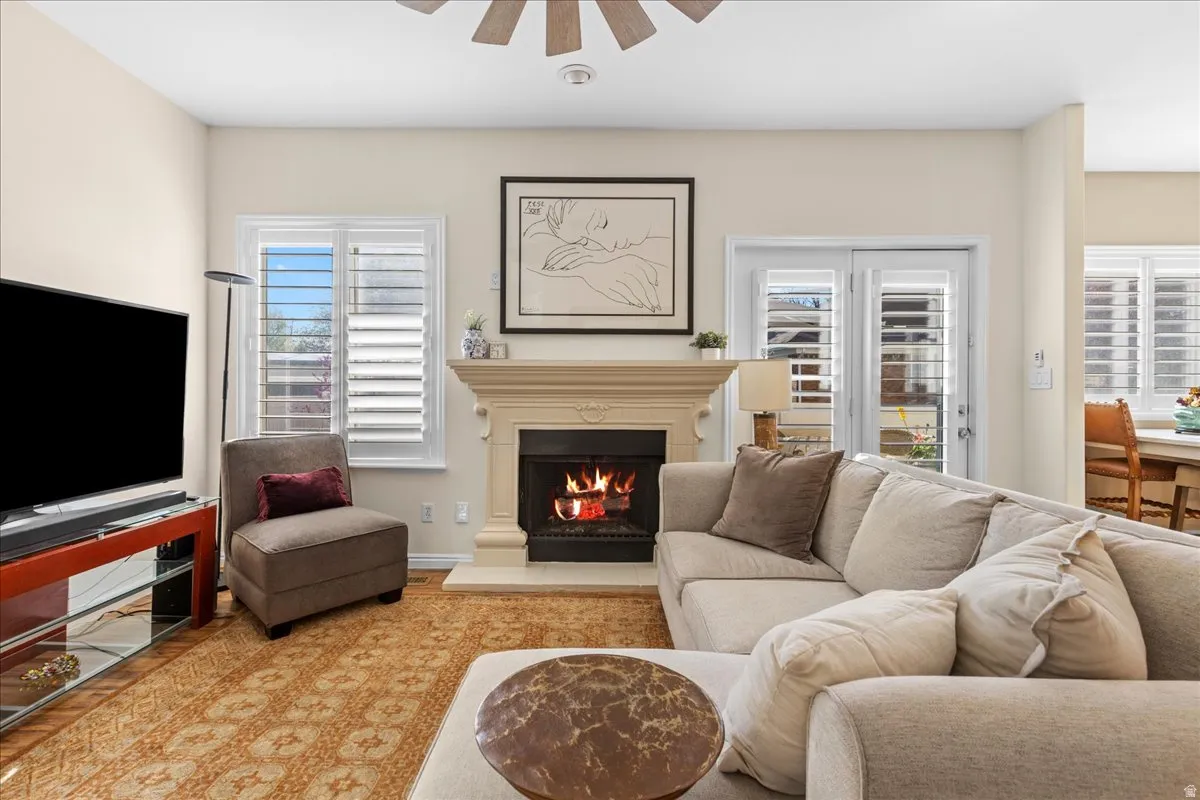 Living area with ceiling fan, a lit fireplace, and wood finished floors