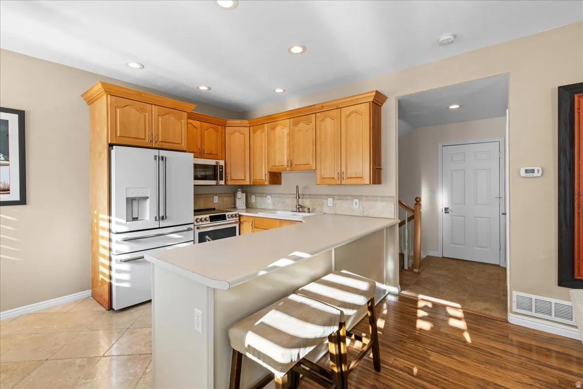 Kitchen featuring high end white refrigerator, light countertops, stainless steel microwave, electric range oven, and a kitchen breakfast bar