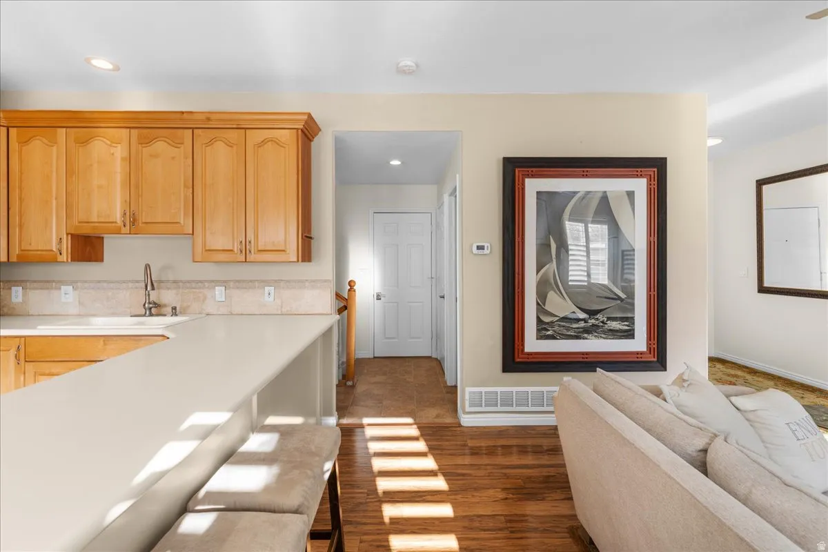 Kitchen with light countertops, dark wood-type flooring, a kitchen breakfast bar, light wood finish cabinetry, and recessed lighting