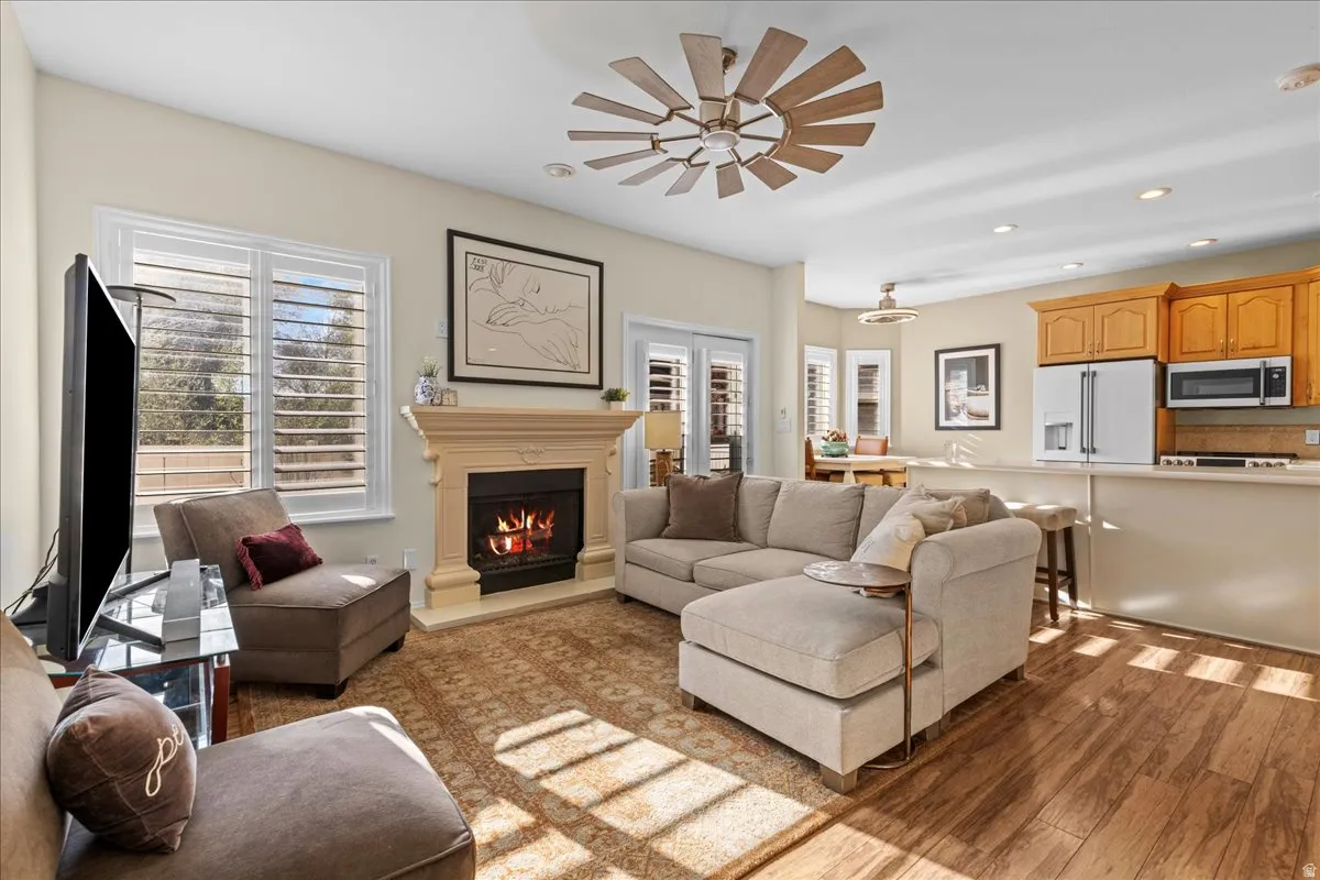 Living room with light wood-type flooring, recessed lighting, a warm lit fireplace, plenty of natural light, and a ceiling fan