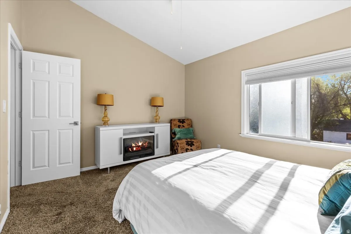Bedroom with lofted ceiling, dark colored carpet, and a glass covered fireplace